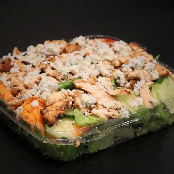 Buffalo Chicken Salad - Seasoned grilled chicken over romaine lettuce with fresh cucumbers, carrots, sweet corn, crumbled blue cheese, and grape tomatoes. Topped with hot sauce and served with blue cheese dressing.